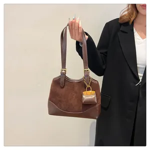 Detail of dark brown suede bucket bag with adjustable strap and mini charm accessory