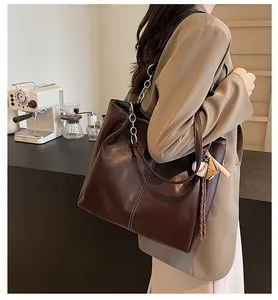 Detalle de bolso tote marrón oscuro con costuras en contraste y colgante de béisbol en café
