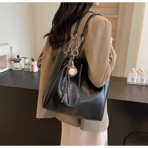 Detalle de bolso tote negro con costuras blancas y colgante de béisbol en correa de cadena