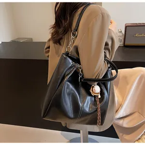 Detalle del bolso tote negro con costuras blancas en contraste y colgante de béisbol