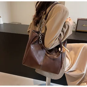 Detalle de bolso tote marrón oscuro con costuras en contraste y amuleto de béisbol