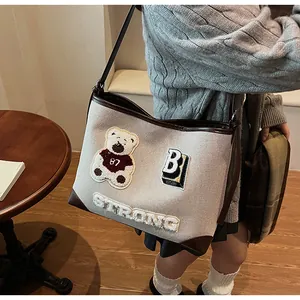 Detail of canvas tote bag showing teddy bear patch and leather trim in a model shot