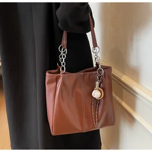 Bolso tote de cuero marrón con costura blanca, correa de cadena plateada y colgante de béisbol