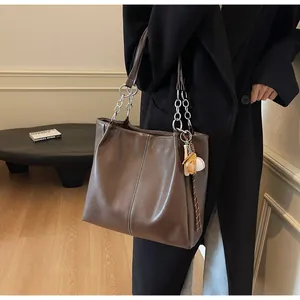 Detalle de un bolso tote de cuero marrón con costuras blancas y un colgante de béisbol