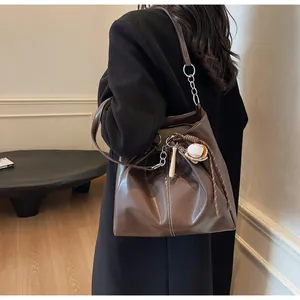 Detalle de bolso de cuero café con pespuntes y colgantes de béisbol en el lateral