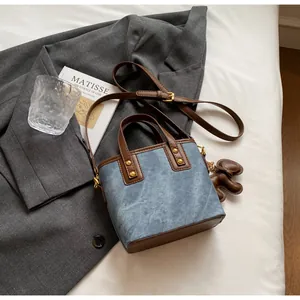 Details einer blauen Tragetasche mit braunem Lederriemen auf grauem Blazer