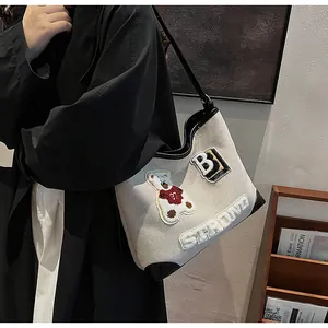 Detail of canvas tote bag featuring embroidered bear patch and black leather trim