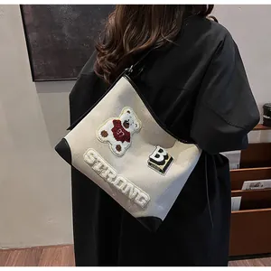 Detail of canvas tote bag featuring teddy bear embroidery and bold STRONG letter patches