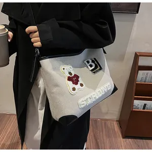 Detail of beige tote bag featuring bear embroidery and STRONG letter patch on canvas