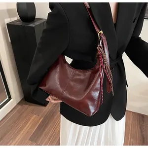 Detail of burgundy shoulder bag with leather texture and woven strap charm accessory
