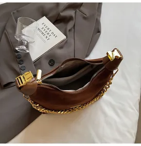 Close-up of brown suede dumpling bag with gold chain strap and interior zipper compartment