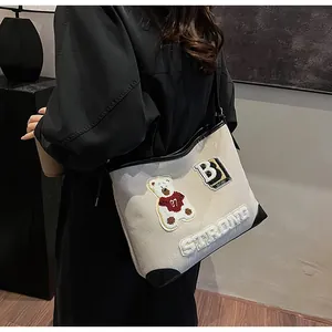 Detail of embroidered bear and B patch on beige canvas tote bag with black leather trim