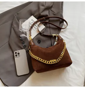 Brown suede hobo bag with thick gold chain detail and leather strap on a grey blazer