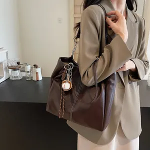 Bolso tote marrón oscuro de piel sintética con costuras blancas y colgante de béisbol