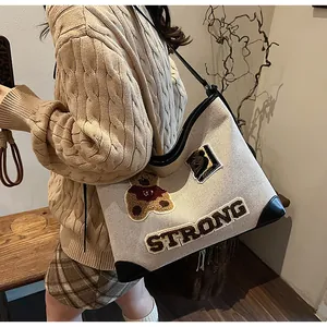 Detail of canvas tote bag featuring plush bear embroidery and black leather trim accents