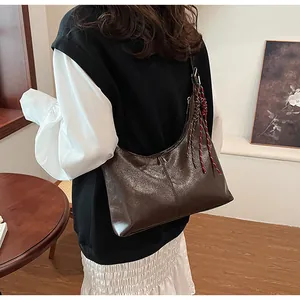 Close-up of a dark brown leather shoulder bag with a stylish red-brown woven rope pendant