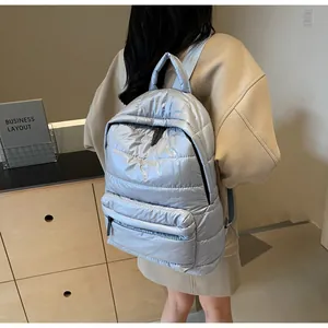 Rear side view of a woman wearing a silver quilted padded backpack in a modern room