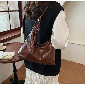 Detail of dark brown glossy leather hobo bag with a red and white woven rope charm