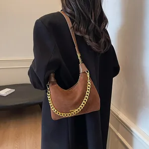Brown suede hobo bag with chunky gold chain strap worn over a black winter coat