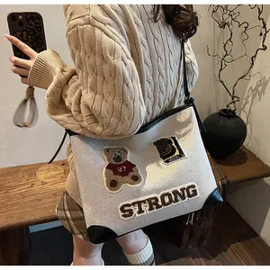 Detail of beige woven tote bag with embroidered bear patch and strong leather corners