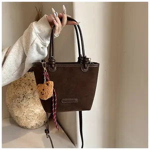 Dettaglio borsa a secchiello in pelle scamosciata marrone con ciondolo a forma di orso