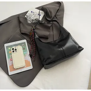 Detail of black faux leather hobo bag with braided tassel on a grey office blazer