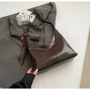 Detail of dark brown hobo bag with glossy finish, ribbon, and key pendant accessory