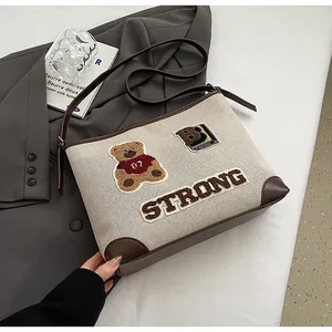Close-up of canvas tote bag with embroidered bear and strong letter patches on the surface