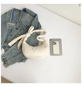 Détail d'un sac demi-lune matelassé blanc crème avec une bandoulière à nœud élégante