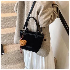 Elegante borsa a secchiello in velluto nero con ciondolo a orsetto, mostrata su modella