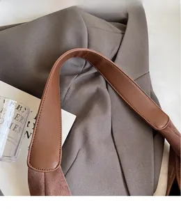 Detail of wide leather shoulder strap with visible stitching on brown matte handbag