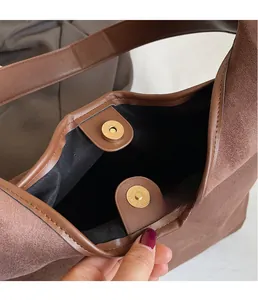Detail of golden magnetic clasp on brown frosted suede tote bag with black lining