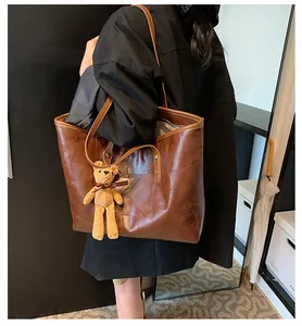 Detail of dark brown leather tote bag with geometric stitching and bear charm