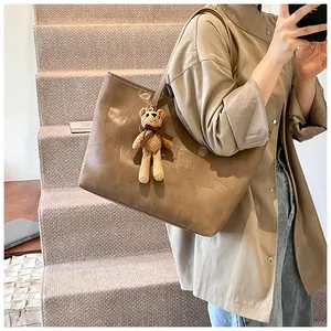 Brown tote bag with square quilted texture and a cute knit bear charm on indoor stairs