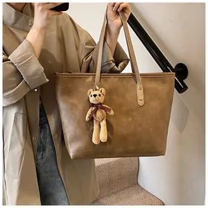 Detail of a large brown tote bag with geometric stitching and a cute bear charm