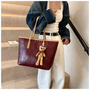Detail of burgundy tote bag with bear charm carried on shoulder by model on stairs