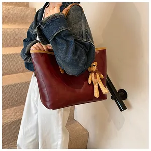 Detailed view of burgundy leather tote bag with contrast stitching and bear charm