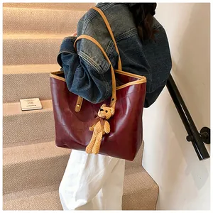 Detail of burgundy leather tote bag with khaki handles and cute yellow bear charm