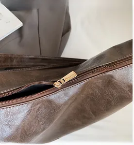 Detail view of the smooth gold-tone metal zipper and textured brown leather shoulder bag