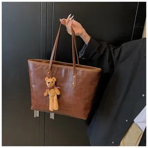 Deep brown textured tote bag with geometric embossing and cute plush bear charm