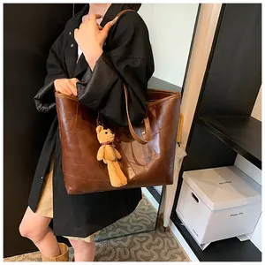 Brown large-capacity tote bag with patchwork texture and teddy bear charm on model
