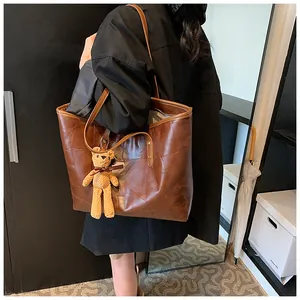 Detail of dark brown faux leather tote bag with stylish bear charm for daily commute