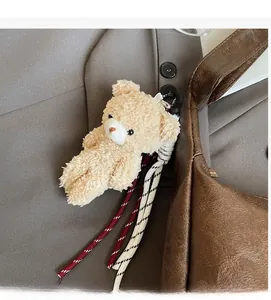 Detail of cute beige plush bear pendant with striped ropes on a brown leather shoulder bag
