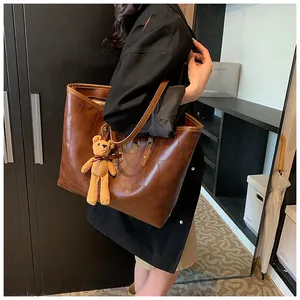Detail of a large brown tote bag with decorative stitching and a plush bear charm