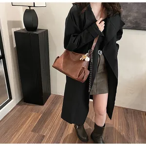 Dettaglio di una borsa a secchiello retrò marrone con ciondoli su un trench nero elegante