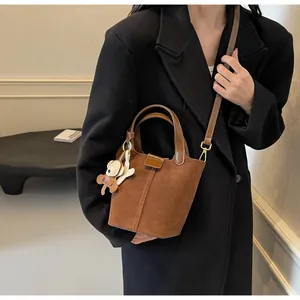 Detail of a brown suede bucket bag featuring golden hardware and a cute bear bag charm