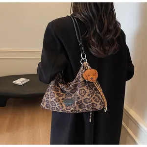 Detail of leopard print tote bag with plush dog charm and braided cord on black strap