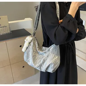 Nahaufnahme der silbernen Plissee-Hobo-Tasche mit einem weißen Plüschbär-Anhänger