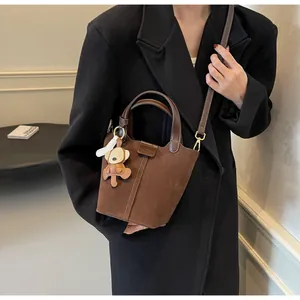 Detail of dark brown suede bucket bag with leather handle and cute monkey charm