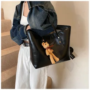 Detail of black patchwork leather tote bag with stylish bear pendant on shoulder strap